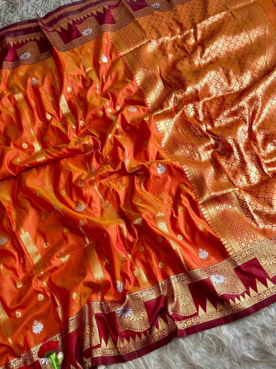 A fiery orange luxurious silk saree of burgundy shade boarder and golden zari of large floral panels with blouse